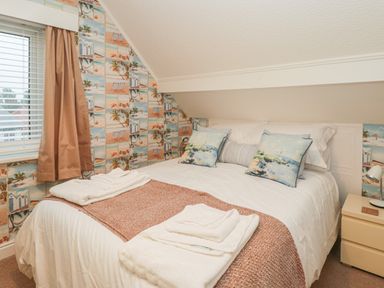 A bedroom with a double bed white bedding folded towels bedside table and window with curtains at Hillcrest in Scarborough
