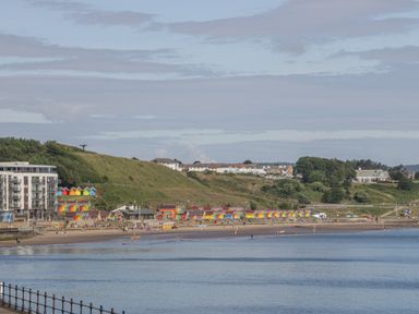 A beach with colorful beach huts and people near the water at Hillcrest in Scarborough