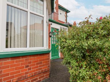 A front entrance with a green door and green framed window beside a brick wall and large leafy bushes at Hillcrest Scarborough