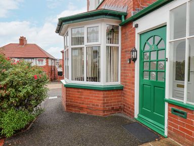 Front entrance of a red brick house with a green door and bay window with curtains and a bush with flowers near the pathway at Hillcrest in Scarborough
