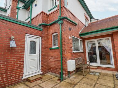 A brick-walled courtyard with a white door wooden bench and glass sliding doors at Hillcrest in Scarborough