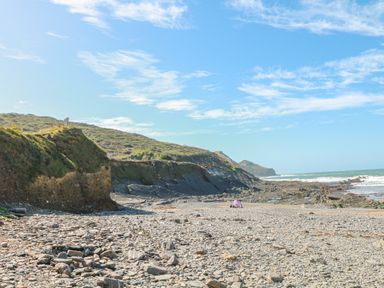 A rocky beach with hills in the background and a small tent near the shore at Little Lanes in Boscastle