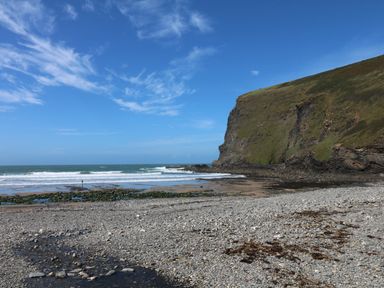 A rocky beach with waves and a large cliff under a blue sky at Little Lanes in Boscastle