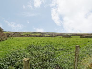 A green field with a wire fence and wooden posts under a partly cloudy sky at Little Lanes in Boscastle