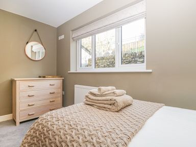 A bedroom with folded towels on a bed next to a chest of drawers and a round mirror at Bishop Fell in Newby Bridge