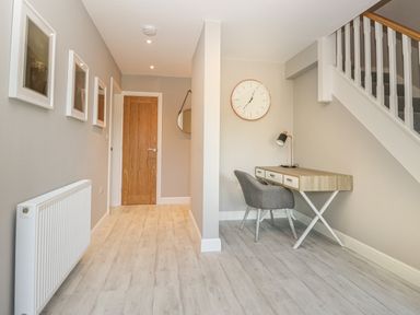 A hallway with a wooden door three framed pictures a radiator a desk a chair a clock and stairs at Bishop Fell in Newby Bridge