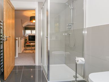 A bathroom with a glass shower enclosure and a view into a carpeted room with a television at Bishop Fell in Newby Bridge