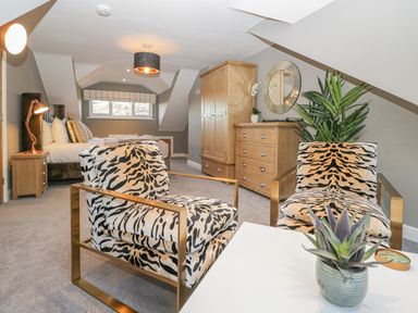 A bedroom with two patterned armchairs a bed wooden furniture and a plant at Bishop Fell in Newby Bridge