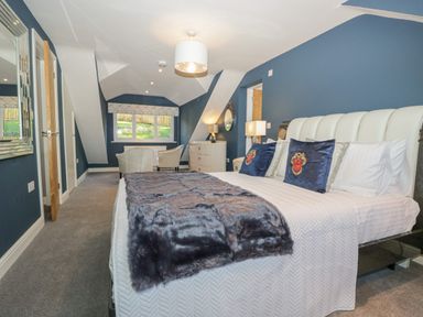 A bedroom with a large bed with pillows and a blanket a pair of chairs near a window and blue walls at Bishop Fell in Newby Bridge