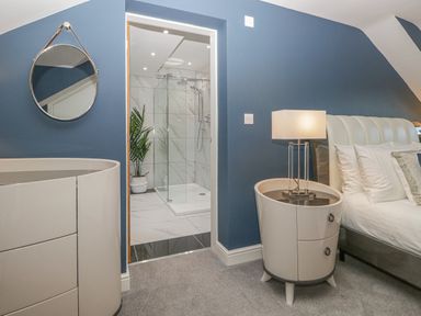 A bedroom with a bed bedside table lamp round mirror and an en suite bathroom with a glass shower at Bishop Fell in Newby Bridge