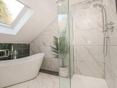 A bathroom with a freestanding bathtub shower area with glass panel tiled walls and a skylight window at Bishop Fell in Newby Bridge