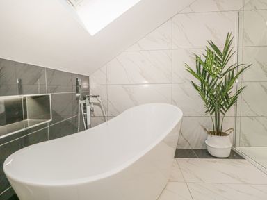 A bathroom with a freestanding bathtub faucet water flowing and a potted plant at Bishop Fell in Newby Bridge