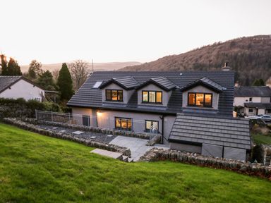 A house with three dormer windows on the roof and a fenced patio area on a grassy hillside at Bishop Fell in Newby Bridge