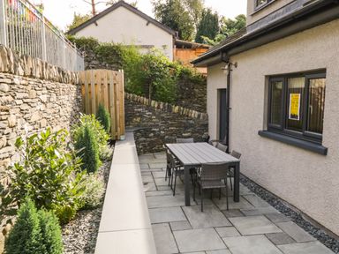 An outdoor patio area with a dining table and chairs next to a stone wall and house at Bishop Fell in Newby Bridge