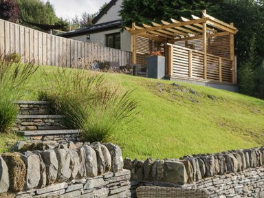 A garden with stone walls steps grass and a wooden pergola at Bishop Fell in Newby Bridge
