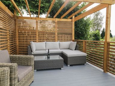 An outdoor seating area with a wicker sectional sofa and armchair under a wooden pergola at Bishop Fell in Newby Bridge