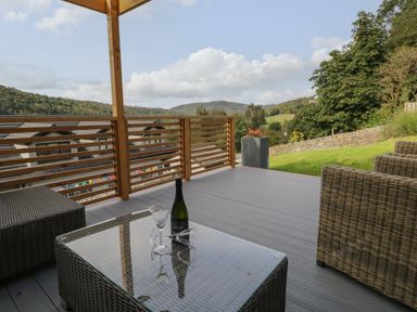 An outdoor patio with wicker furniture and a glass table with a wine bottle and glasses at Bishop Fell in Newby Bridge