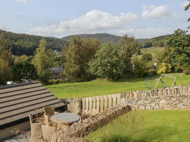 A garden with outdoor furniture a stone wall and playground equipment in a rural landscape at Bishop Fell in Newby Bridge