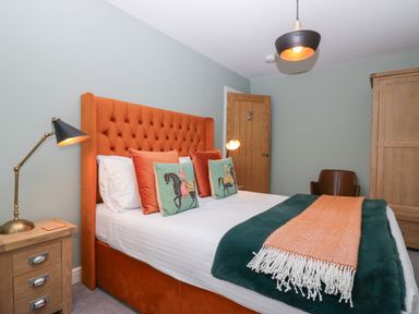 A bedroom with an orange upholstered bed and matching pillows a wooden bedside table with a lamp a wooden door a brown chair and a wooden wardrobe at Bishop Fell in Newby Bridge