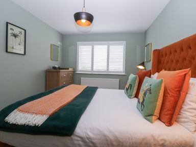 A bedroom with a bed with orange headboard and decorative pillows a chest of drawers and a window with shutters at Bishop Fell in Newby Bridge