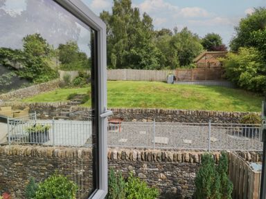 View of a garden with stone walls grass and a wooden pergola from an open window at Bishop Fell in Newby Bridge