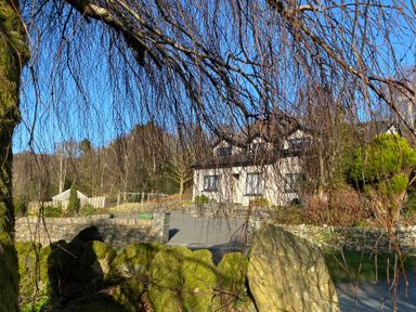 A house with a stone wall and driveway surrounded by trees and bushes at Bishop Fell in Newby Bridge