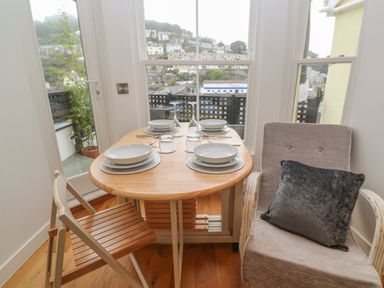 A dining table set for four with plates and glasses next to a window and two chairs at 1 River View in Looe