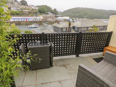A balcony with a wicker table and chairs overlooking a river with boats and buildings at 1 River View in Looe