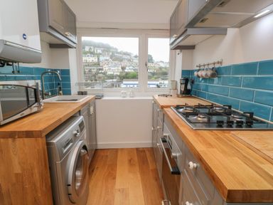 A kitchen with wooden countertops blue tiled backsplash a washing machine microwave stove and a window showing houses outside at 1 River View in Looe