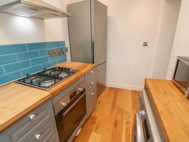 A kitchen with wooden countertops blue tile backsplash grey cabinets a gas stove oven refrigerator microwave and washing machine at 1 River View in Looe