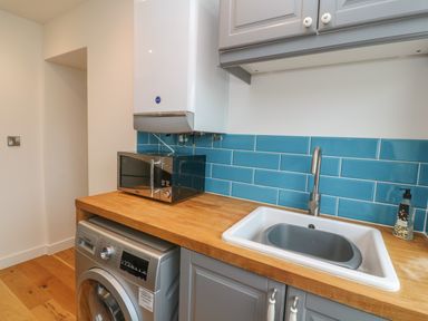 A utility room with a washing machine microwave wooden countertop white sink and blue tiled backsplash at 1 River View in Looe