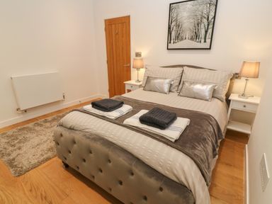 A bedroom with a double bed two bedside tables with lamps a wooden door and a rug on the floor at 1 River View in Looe