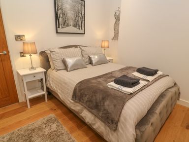 A bedroom with a double bed with folded towels on it two bedside tables with lamps and a framed picture above the bed at 1 River View in Looe