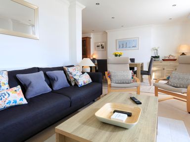 A living room with a dark sofa with cushions two armchairs a wooden coffee table and a dining table at 2 Embankment House in Dartmouth