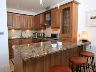 A kitchen with wooden cabinets a marble countertop bar stools and kitchen appliances at 2 Embankment House in Dartmouth