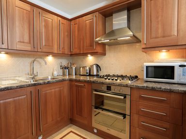 A kitchen with wooden cabinets a gas stove a microwave kettle toaster and sink at 2 Embankment House in Dartmouth