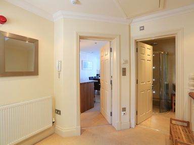 A hallway with two open doors one leading to a kitchen and dining area the other to a bathroom with a shower at 2 Embankment House in Dartmouth