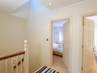 A hallway with a staircase and two open doors leading to bedrooms at 2 Embankment House in Dartmouth