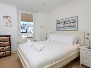 A bedroom with a white bed and rolled towels on top a window a chest of drawers and a framed painting on the wall at 2 Embankment House in Dartmouth