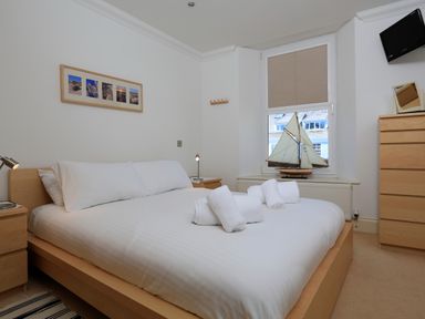 A bedroom with a bed with white linens and rolled towels a model sailboat on the windowsill and wooden furniture at 2 Embankment House in Dartmouth