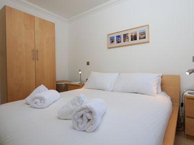 A bedroom with a double bed three rolled white towels on the bed wooden wardrobe bedside tables and a picture frame on the wall at 2 Embankment House in Dartmouth