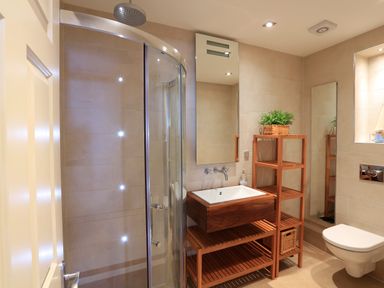 A bathroom with a glass shower enclosure wooden shelves and a white sink at 2 Embankment House in Dartmouth