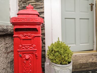 A red postbox next to a door and a potted plant at The Postmasters House in Windermere