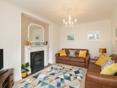 A living room with brown leather sofas yellow cushions a patterned rug fireplace and a chandelier at The Postmasters House in Windermere