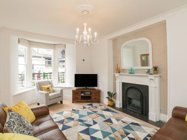 A living room with a leather sofa armchair TV and fireplace at The Postmasters House in Windermere