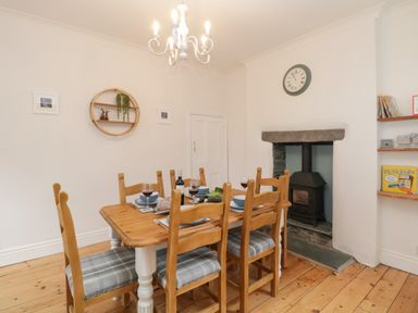 A dining room with a wooden table and six chairs by a fireplace at The Postmasters House in Windermere