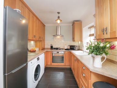 A kitchen with wooden cabinets refrigerator washing machine oven and flowers on counter at The Postmasters House in Windermere