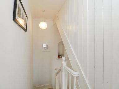 A staircase with white paneling a hanging light and framed pictures at The Postmasters House in Windermere