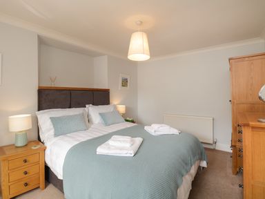 A bedroom with a double bed with blue covers and white towels on the bed with wooden furniture at The Postmasters House in Windermere