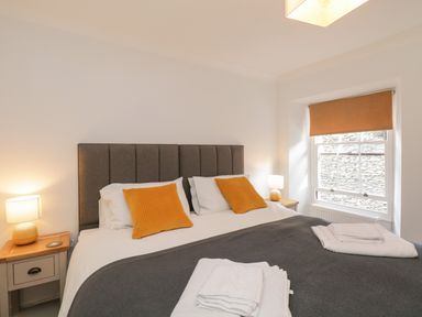 A bedroom with a double bed with orange cushions bedside tables with lamps and a window with an orange blind at The Postmasters House in Windermere